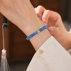 Detail view of blue obsidian beaded bracelet worn with floral embroidery sleeves