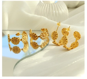 Detailed view of matte gold daisy earrings with floral patterns on white silk fabric