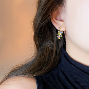 Detail of elegant gold horse stud earring with blue and yellow crystals on a model