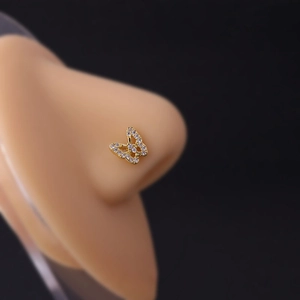 Macro detail of a golden butterfly nose stud with white zircon on a silicone model