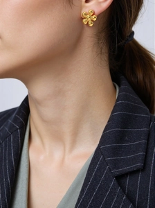 Gros plan d'une boucle d'oreille fleur dorée portée par un mannequin, design minimaliste