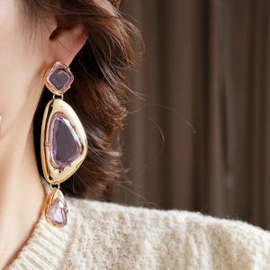 Detail of vintage gold earrings with irregular purple crystals on a female model