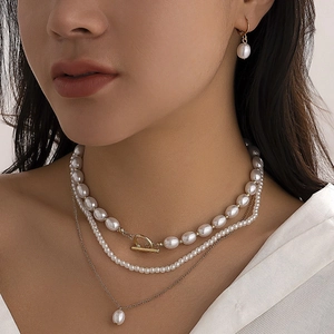 Close-up of layered faux pearl necklace set with heart charm and matching earrings on a model
