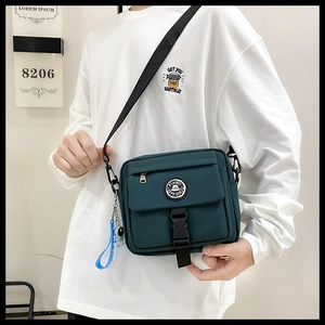 Detail of dark green nylon messenger bag with buckle and blue space theme pendant