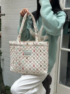 Outdoor lifestyle shot of a white quilted tote bag with floral bear patterns and logo