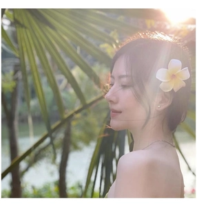 Close-up of a white plumeria flower hair clip worn by a model in tropical sunlight
