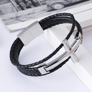 Detailed view of men's braided leather bracelet with a polished silver cross on a white pedestal