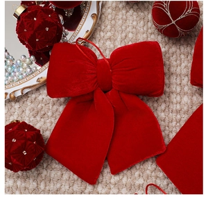Close-up of red velvet Christmas bow with gold ornaments on woven background
