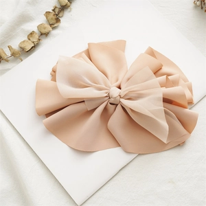 Close-up of beige multi-layer fabric and chiffon bow hair clip on a minimalist background