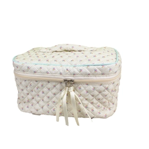 Floral quilted cosmetic bag with beige handle and ribbon zipper closure on white background