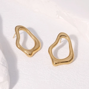 Détail de boucles d'oreilles irrégulières en acier doré sur fond texturé blanc