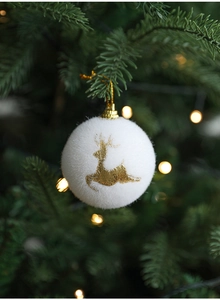 White flocked Christmas ball with gold elk print hanging on a decorated Christmas tree