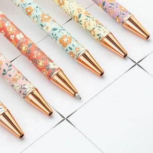 Floral pattern retractable metal ballpoint pen with rose gold trim on grid paper