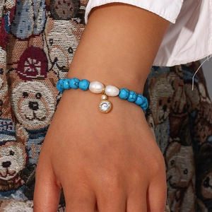 Close-up of blue turquoise beaded bracelet with white imitation pearls and gold zircon charm