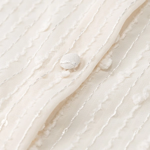 Close-up of beige jacquard blouse with silver embroidery, pom-pom stripes and fabric button