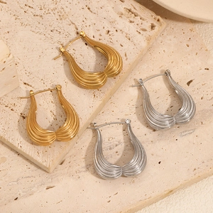 Close-up of gold and silver U-shaped earrings with striped texture on stone surface