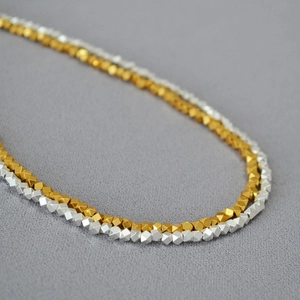 Macro shot of gold and silver faceted geometric beads on a minimalist brass necklace
