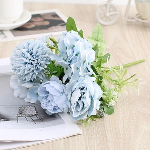 Detail of light blue faux peonies and chrysanthemums on a wooden desk with a coffee cup