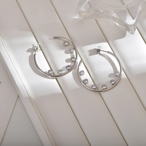 Close-up of silver hoop earrings featuring sparkling cubic zirconia insets on a white stand