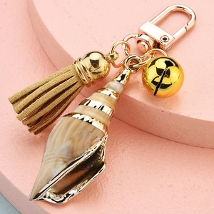 Close-up of conch shell keychain with gold bell, suede tassel and lobster clasp