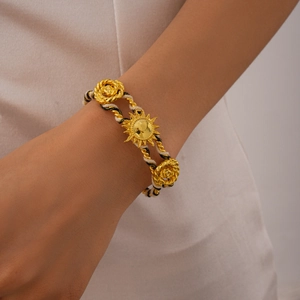 Macro shot of gold sun and rose charms on a woven tricolor cord bracelet for women