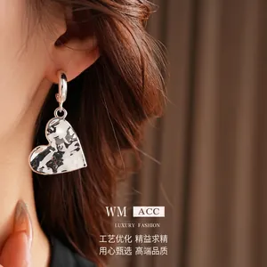 Silver hammered heart pendant C-shape hoop earrings worn by a model against a textured fabric