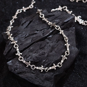 Vintage silver fleur-de-lis and cross chain necklace displayed on dark textured stone