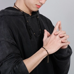 Dettaglio di collana e bracciale neri stile street indossati da un modello uomo