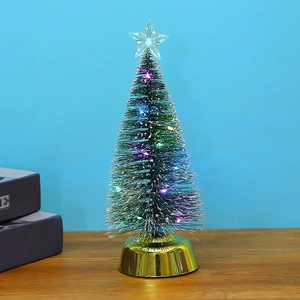 Close-up of mini glowing Christmas tree with LED lights and golden base on table