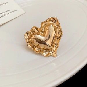 Detailaufnahme eines goldenen Herzrings mit eleganter Faltenstruktur auf einem Tablett