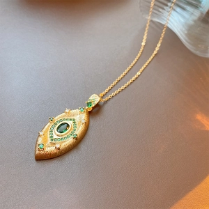 Macro shot of gold eye-shaped pendant with green stones and textured finish detail