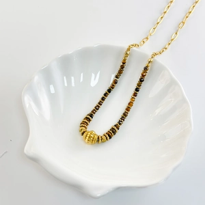 Macro detail of natural tiger eye beads and striped gold bead in a ceramic shell tray