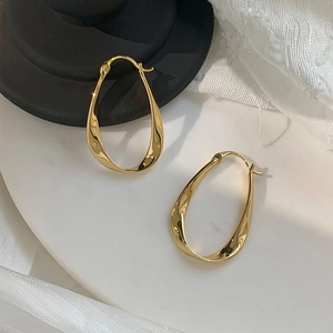 Elegant gold twisted oval hoop earrings displayed on a white marble surface backdrop