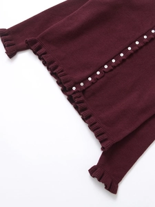Detailed macro view of burgundy knit cardigan featuring white buttons and ruffled hem details