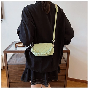 Detail of light green ruffled crossbody bag with gold studs and quilted texture on model