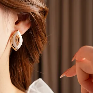 Vintage gold leaf-shaped earrings with white enamel finish on female model