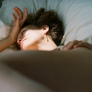 Close-up of elegant gold teardrop earrings worn by a model resting on a white pillow