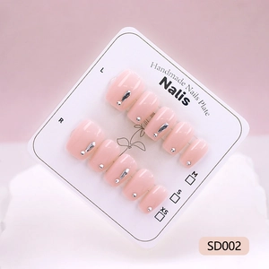 Faux ongles faits main rose poudré avec détails métalliques argentés sur une carte blanche