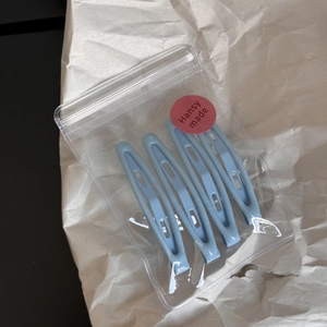 Detail of four light blue teardrop metal hair clips neatly packed in a clear zipper bag