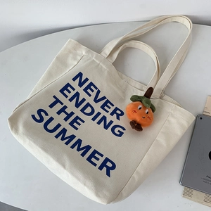 Detail of canvas tote bag with blue text and orange persimmon charm on grey desk