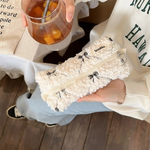 Close-up of fluffy white fleece pouch with black bow print and metal zipper ring