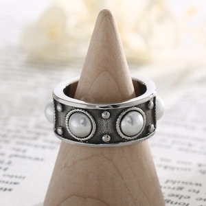 Détail macro d'une bague argentée vintage avec perles et clous texturés sur support en bois