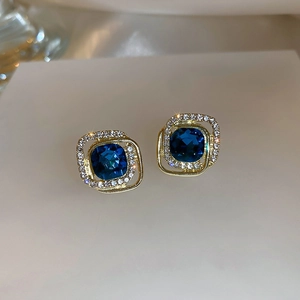 Macro detail of luxury golden square earrings with navy blue gemstone and shimmering diamonds