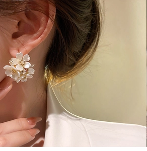 Dettaglio degli orecchini a C con fiori bianchi e perle dorate indossati da una modella