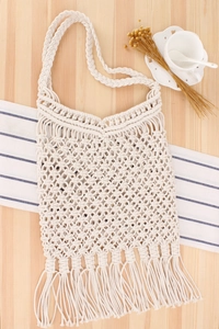 Detail of bohemian handmade hollow woven beach bag with long tassels on wooden surface
