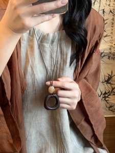 Detail of wooden resin pendant necklace worn by model against Chinese calligraphy background