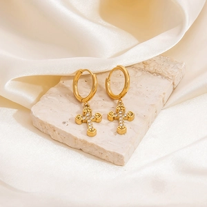 Detailed view of gold cross drop earrings with pavé zircons on marble and silk background