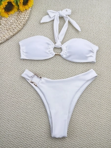 Flat lay of white halter bikini set with gold metal rings on a summer beach mat