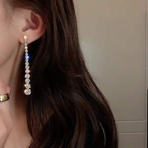 Macro detail of long silver tassel earrings featuring sparkling rhinestones on a model