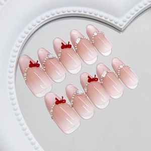 Pink cat eye gradient press-on nails with 3D bows and pearls on a display tray